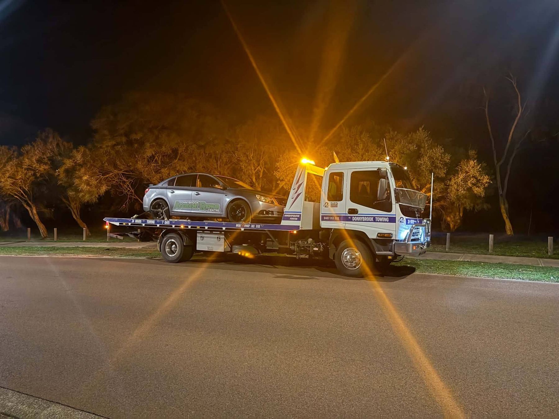 Tilt tray with amber beacons on, loading a car at night