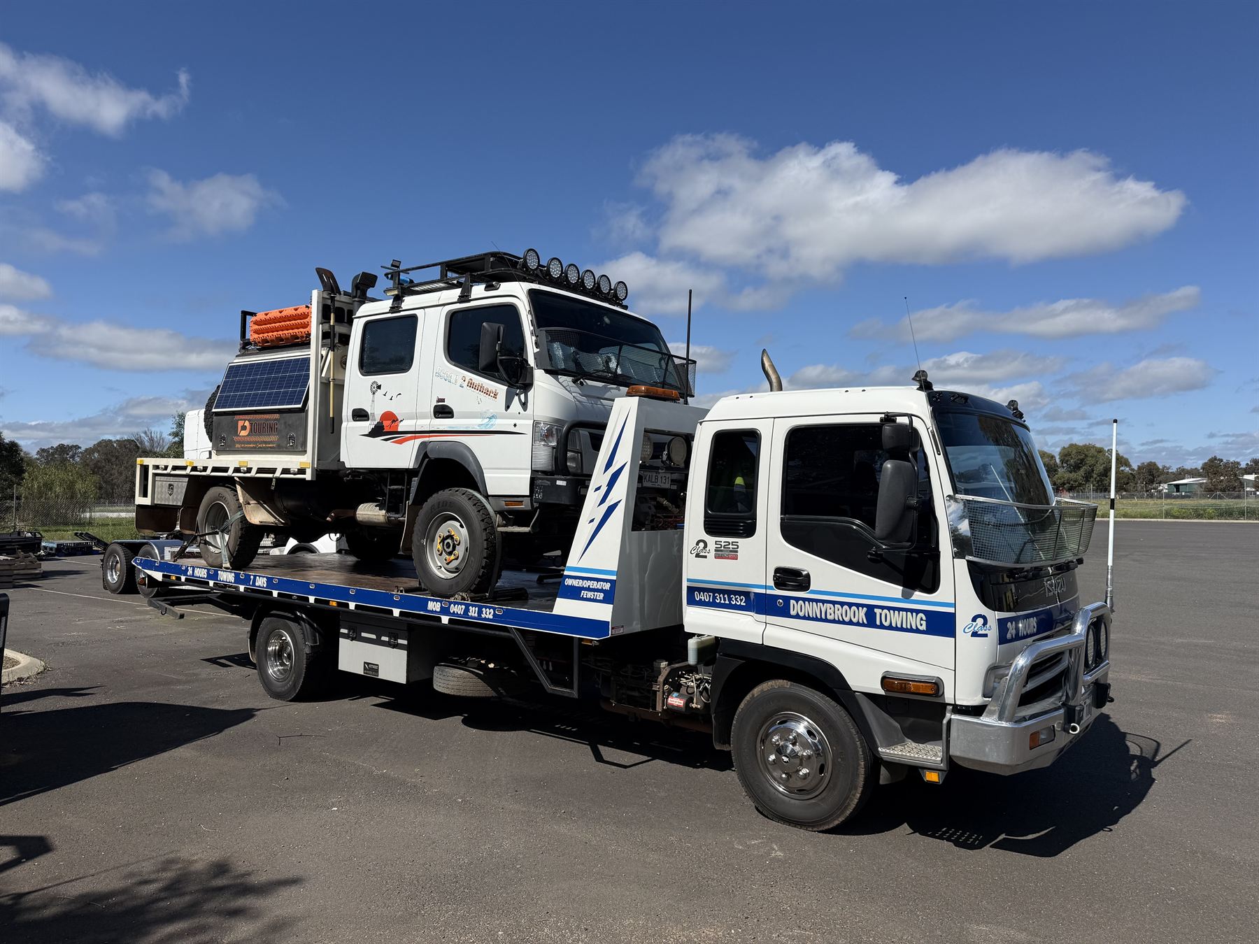 The white Donnybrook Towing Isuzu tilt tray carrying a 4x4 expedition truck